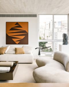 Modern, minimalist living room featuring a white fabric sofa, abstract art, and a view of the city through large windows.