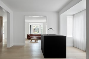 Modern interior design featuring a black kitchen island with a white countertop, contrasting light-colored wood floors, and a