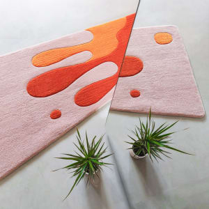 A modern-style textured rug with abstract shapes in shades of orange and peach placed on a smooth, light-colored floor with t
