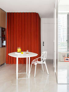 A minimalist kitchen featuring a white metal table and chair with a red curtain and white door in the background.
