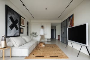 Modern minimalist living room with white furniture, a large TV, and framed art on the walls.