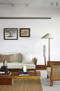 A minimalist living room featuring a wooden sofa, fabric cushions, and a glass coffee table.