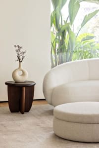 A modern living room featuring a textured fabric sofa and a wooden side table with a vase holding small flowers.