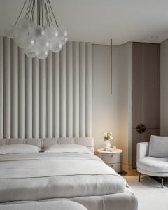 A modern bedroom with white walls and bed, featuring a white chandelier and a side table with a vase of flowers.