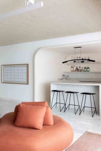 Spacious modern living room with large circular peach-colored lounge chair and concrete bar area with shelves and black stool