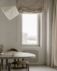 Neutral-toned minimalist dining room with a round wooden table, wooden chairs, and a simple decorative plant in a vase.