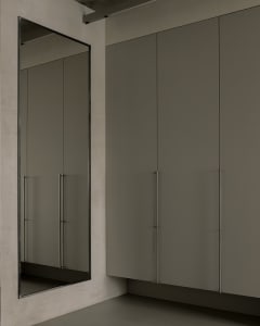 A minimalist interior design featuring a concrete wall and floor, with a large mirror and a cabinet.