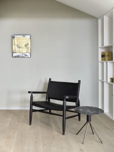 A modern living room featuring a black leather armchair with a marble side table, against a neutral wall with an abstract pai