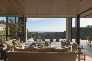 Modern patio with minimalist design featuring wooden and glass panels and concrete elements, overlooking a scenic hillside.