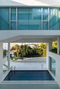 Modern building with glass walls and a rooftop pool overlooking greenery.