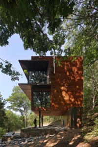 A modern treehouse with wooden siding and large windows surrounded by trees.