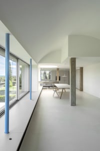 Modern minimalist living room with concrete walls and floor, large windows, and simple furniture.