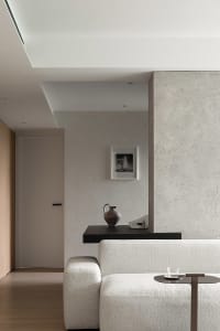 A minimalist living room with concrete walls, a white sofa, and a coffee table with a glass cup.