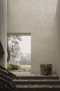 Modern exterior view of a building with a textured concrete wall and a pathway leading to a garden.