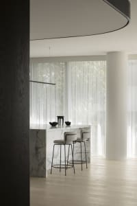 A modern kitchen interior featuring a marble counter and wooden stools.