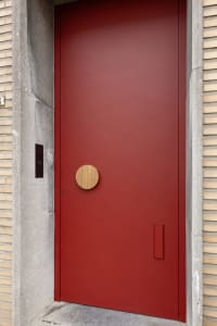A sleek, red, metallic front door with a unique wooden circle handle.