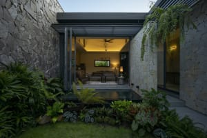 A modern living space with concrete walls and a glass wall, featuring a cozy seating area and a small indoor pool with surrou
