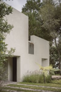 A minimalist modern exterior house with a concrete facade and greenery surrounding it.
