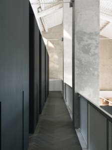 Modern industrial office hallway with concrete walls, herringbone wood floor, and concrete ceiling beams.