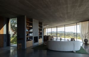 Modern living room with concrete walls, floor, and ceiling, featuring a large circular sofa and a bookshelf filled with books