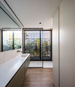 A modern bathroom with glass walls and wooden flooring, featuring a large window with a view of greenery.