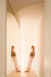 A person standing in a minimalist corridor with neutral tones.