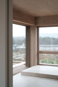 Minimalist architectural space with large windows featuring wooden frames and flooring.