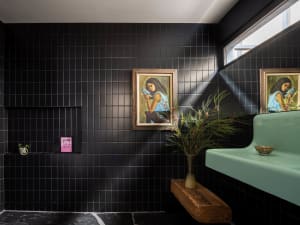 A modern minimalist bathroom with black tiled walls, concrete floor, and green plants