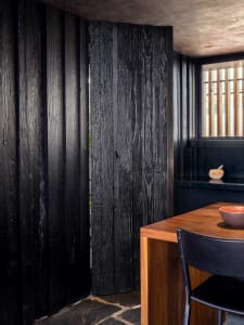 A modern kitchen with charred-wood walls and a wooden table.