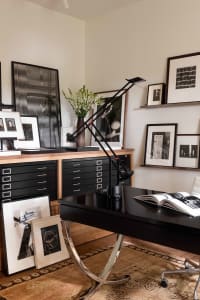Industrial-style office with metal desk and black filing cabinet inside a room featuring multiple framed photographs on the w