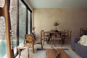 A minimalist residential interior featuring a wooden dining table, chairs, and a sofa in a room with a stone wall and a glass