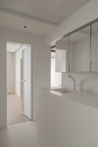 A minimalist white bathroom with a single sink, mirror, and cabinet.