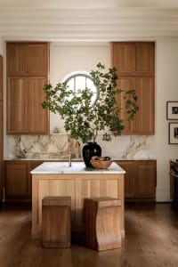 A modern residential kitchen featuring a wooden island with a marble countertop and a round window.