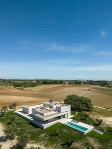A modern villa with a concrete exterior, featuring a swimming pool and surrounded by greenery.