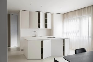 Modern, minimalist kitchen with white cabinets and countertops, featuring a sleek design and a small window.