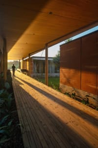 A person walking on a wooden pathway in a modern patio setting with greenery and a building exterior in the background.