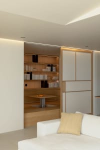 A modern minimalist living room featuring a white couch, a wood coffee table, and a bookshelf filled with books.