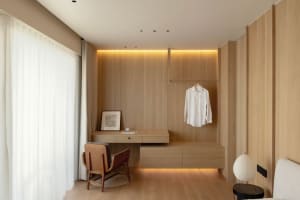 Modern bedroom with wooden furniture, white shirt hanging on wall, and desk with draws.