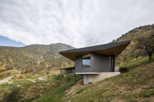 A modern house with a flat roof, built into a hillside, featuring concrete and wood materials.