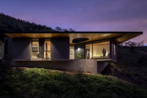 Modern residential house exterior during twilight with wooden and concrete exterior and large glass windows.