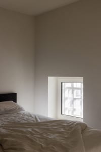 A minimalist bedroom with a white bed and textured wallpaper.