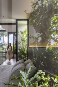 A minimalist bedroom featuring greenery, with a person walking through the space.