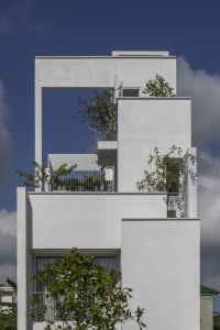 A minimalist white building made of concrete with plants on the upper levels.