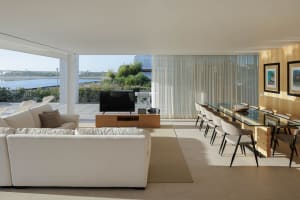 Modern living and dining room featuring mixed materials with a glass dining table, wooden TV stand, and white sofas with scen