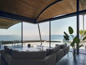 Modern living room featuring concrete walls and floor with large glass windows overlooking the ocean.