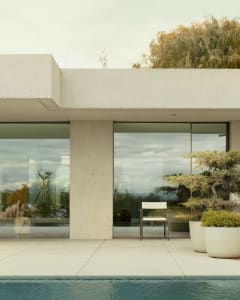 A modern minimalist patio with concrete walls and floor, large glass windows, and a single white chair.