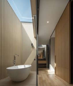 Modern minimalist bathroom with a white stand-alone tub set against a wooden floor and wall, featuring a skylight for natural