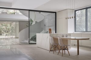 A minimalist kitchen featuring a marble island with two transparent chairs and a large window.