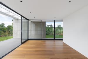Modern minimalist living room with concrete walls, large glass windows, and wooden flooring.