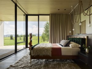 A modern bedroom featuring a bed with green and red bedding, a wooden headboard, and a large window overlooking green fields 